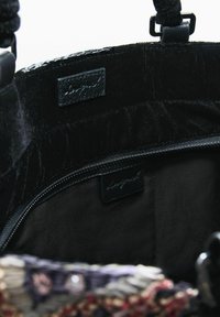 Indvendig udsigt af en sort håndtaske, der viser en lynlåslomme med stofforing og to små lædermærker indeni.