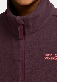 Veste en polaire de couleur violet foncé avec un col montant. Équipée d'une fermeture éclair à l'avant et d'un logo rose. Texture douce, adaptée à une utilisation en extérieur.