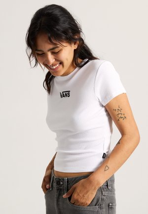 White ribbed short-sleeve t-shirt with Vans logo, fitted design, round neckline, paired with gray jeans, featuring visible stitching and pockets.