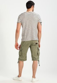 Pruhované béžové a námořnické tričko v kombinaci s olivovými cargo šortkami se bočními kapsami a šňůrkami. Bílé tenisky dokončují outfit.