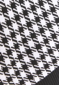 Černo-bílá látka s houndstooth vzorem, texturované pletení, s malými, opakujícími se zigzagovými tvary v kontrastní barevné schématu.