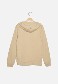 Sudadera con capucha beige colgada en una percha de madera. Presenta una textura suave, mangas largas y un diseño simple sin acentos visibles.