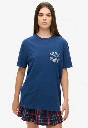 Navyblauwe katoenen t-shirt met korte mouwen en een ronde hals, met een witte "Superdry" grafische print. Gecombineerd met een geruite minirok in rood en groen.