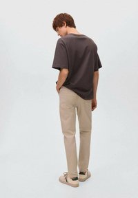 Camiseta de corte suelto en gris oscuro, pantalones de mezclilla beige y zapatillas de color claro con acentos verdes. Diseño sencillo, estilo casual, sin patrones visibles.