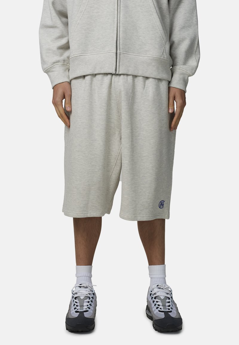 Shorts gris en mélange de coton avec une taille élastique, des poches latérales et un petit logo bleu sur le côté gauche. Portés avec des baskets grises et des chaussettes blanches.