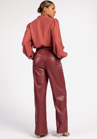 Rostfarbige Bluse mit puffärmel und Rüschenausschnitt, kombiniert mit hochgeschnittenen, burgunderfarbenen Lederhosen mit glatter Textur.