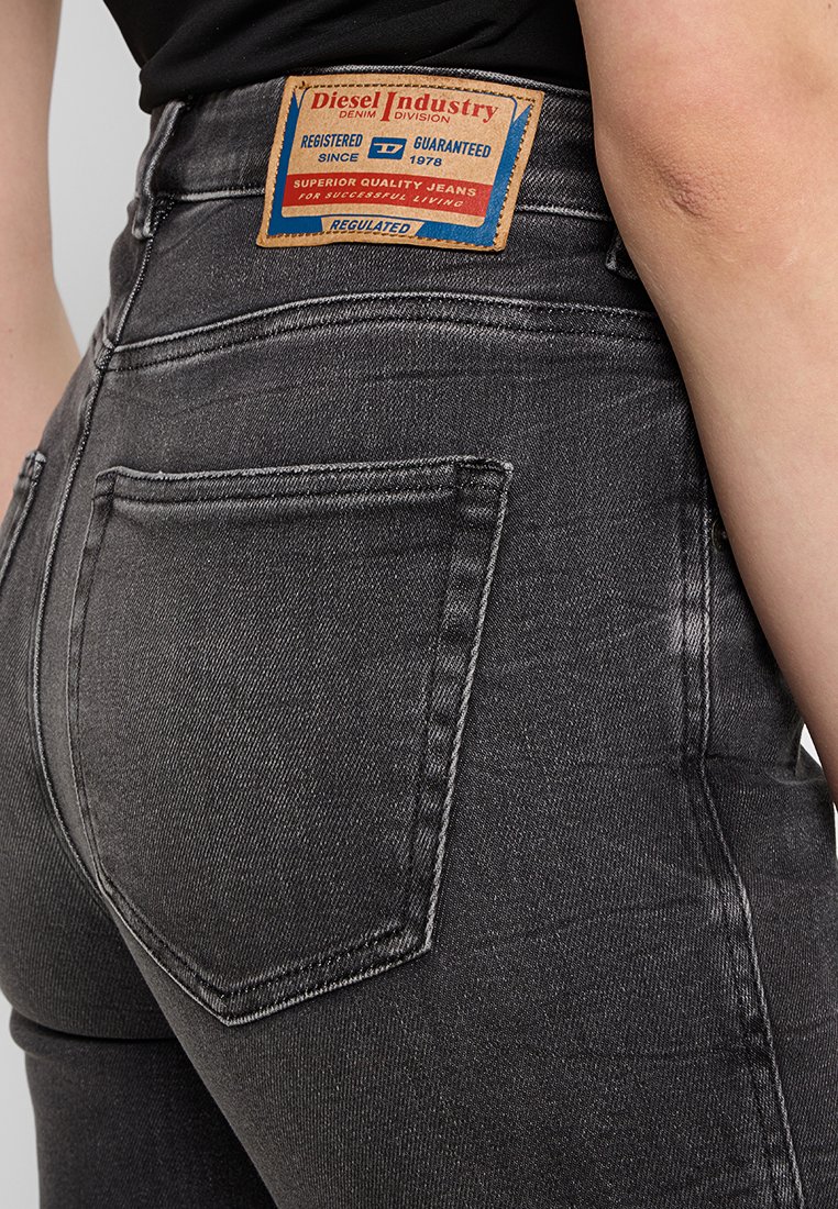 Nahaufnahme einer Person, die dunkelgraue Diesel-Jeans trägt, mit einem sichtbaren, gebrandeten Lederpatch über der Gesäßtasche.