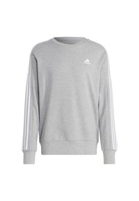 Siva sweatshirt iz mehkega blaga, s krožnim izrezom, dolgimi rokavi in belimi tremi črtami, ki se spuščajo po ramenih. Prikazana je Adidasova blagovna znamka.
