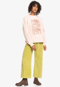 Lys rosa oversized sweatshirt med grafisk trykk, kombinert med høyt liv olivenfargede kordfløyelsbukser og brune ankelstøvler.