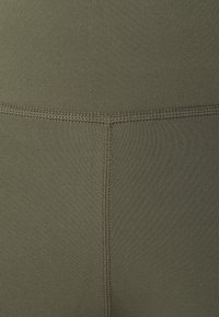 Leggings verde oliva realizzati in un tessuto morbido e elasticizzato. Presentano cuciture flatlock e una cintura ampia, offrendo una vestibilità e una finitura confortevoli.