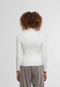 Biały sweter z golfem, prążkowany, z długimi rękawami, dopasowany, z detalem na szwie z tyłu, w zestawie z szarymi spodniami z kordurowej tkaniny.