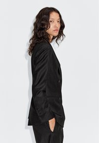 Zwart gestreept op maat gemaakt pak met een gestructureerd ontwerp, een enkelrijige jas en zijzakken. Gladde stof met een lichte glans.