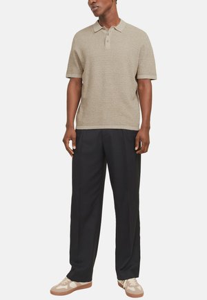 Beige Poloshirt mit kurzen Ärmeln aus strukturiertem Strickstoff, mit einem Knopfverschluss mit drei Knöpfen, getragen zu schwarzen geraden Hosen und beigen Sneakers.