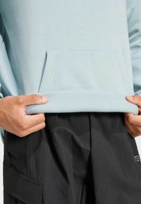 Vaaleansininen huppari, jossa on etutasku ja teksturoitu helma, yhdistettynä löysiin mustiin housuihin, joissa on sivutaskut.