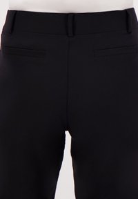 Zwarte broeken van een gladde, rekbare stof, met een aansluitend ontwerp en twee achterzakken. Geen zichtbare patronen of hardware-details.