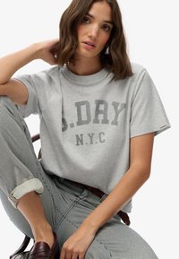 Grijze katoenen T-shirt met korte mouwen, voorzien van een gedurfde "S.DAY N.Y.C" grafische print in donkergrijs. Draagt het met gestreepte broek.