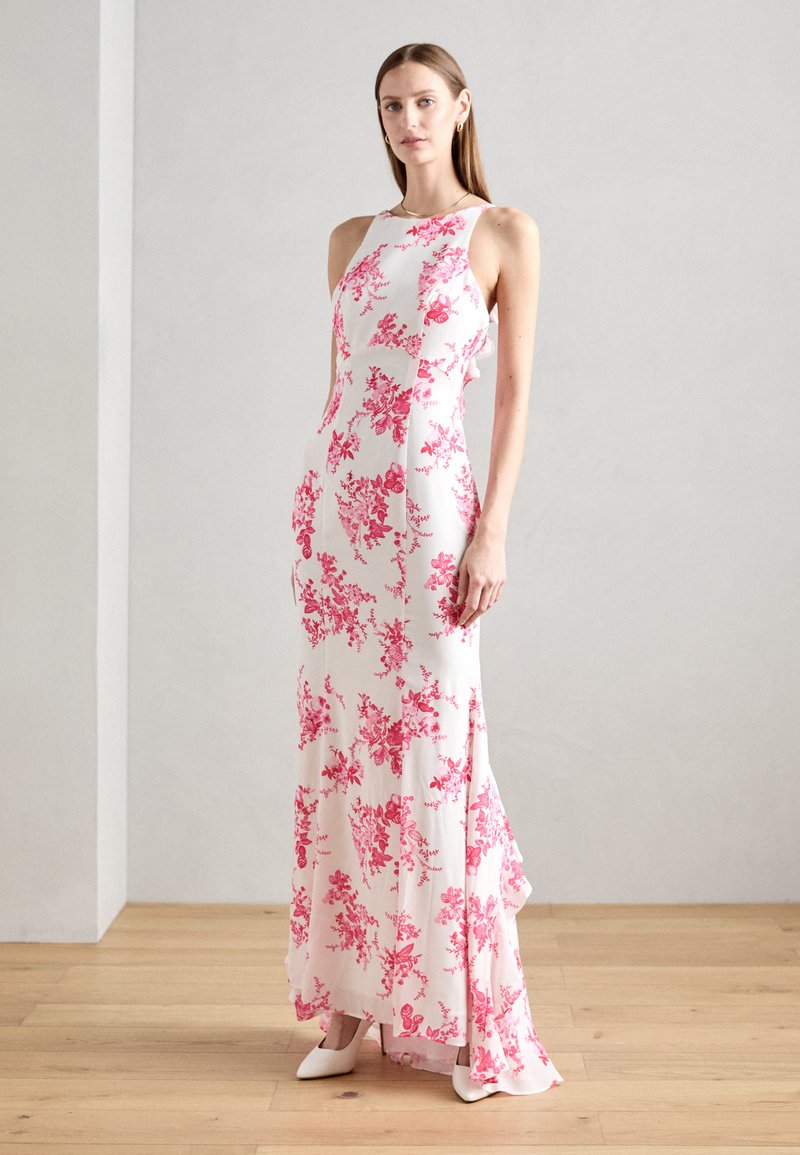Robe maxi blanche à motifs floraux roses, sans manches, en tissu léger avec une légère traîne. Portée avec des talons blancs pointus.