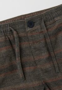 Pantalones de mezcla de algodón con un patrón texturizado en gris oscuro, que presentan rayas rojas y azules, una cintura elástica y un cierre de botón negro.