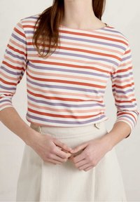 Randig långärmad topp i ljusrosa, orange och lila, med båtformad halsringning och åtsittande ärmar, matchad med en beige kjol.