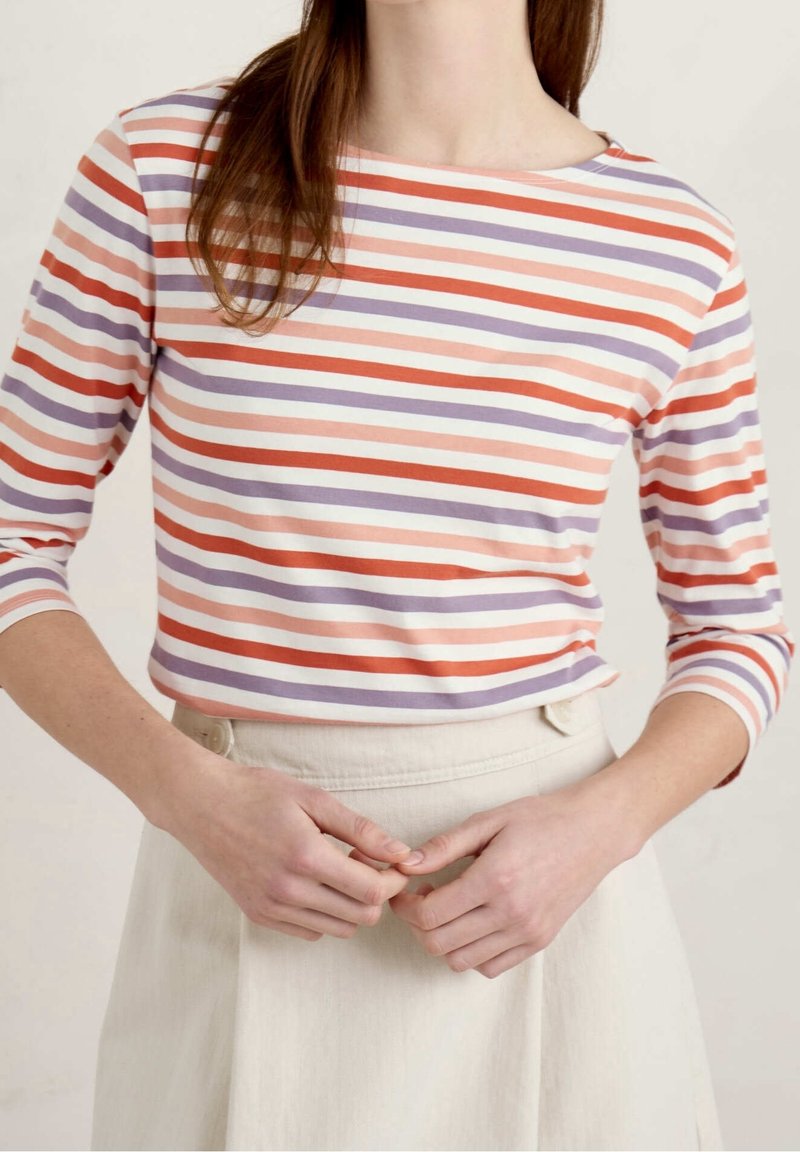 Randig långärmad topp i ljusrosa, orange och lila, med båtformad halsringning och åtsittande ärmar, matchad med en beige kjol.