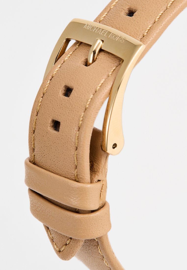 Cinturón de cuero marrón claro con hebilla dorada grabada "Michael Kors" y bordes cosidos, mostrado abrochado con el pasador de la hebilla en un agujero.