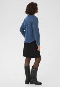 Džinsa jaka vidējā zilā tonī ar garām piedurknēm, noapaļu apakšmalu un izšūtiem akcentiem, kombinēta ar melnu svārku un melniem ādas zābakiem līdz ceļgaliem.