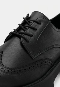 Μαύρο δερμάτινο παπούτσι με ομαλή υφή, σχέδιο με φτερά και τρυπήματα, και στρογγυλά κορδόνια.