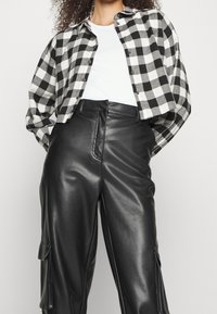 Schwarz-weiß karierte Flanellbluse, im cropped Design, mit Knopfleiste, kombiniert mit hoch taillierten schwarzen Lederhosen mit seitlichen Taschen.