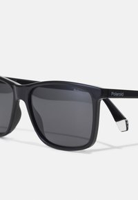 Black plastic sunglasses with dark gray lenses, square design, slightly textured frame, silver-tone accents on temples. Polaroid logo present.