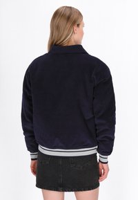 Marine corduroy jas met een kraag, ribgebreide manchetten en een grijs gestreepte zoom. De jas heeft een relaxte pasvorm en een gestructureerde stoffen oppervlak.