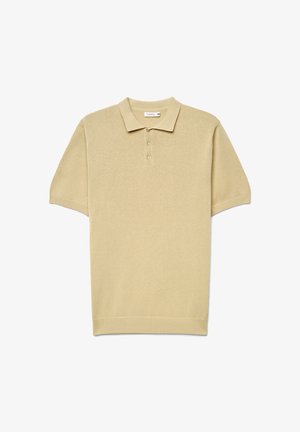 Polo a maniche corte in beige chiaro, realizzata in tessuto lavorato a maglia. Presenta un colletto classico, una patta con tre bottoni e bordi a costine sull'orlo e sulle maniche.