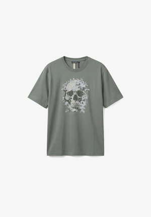 Maglietta a maniche corte verde oliva con un dettagliato disegno di teschio realizzato con fogliame e piante, posizionato al centro sul davanti.