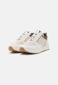 White and beige sneakers with textured fabric, laces, and a side zipper. Features a cushioned sole and gum rubber bottom. Metallic accents present.