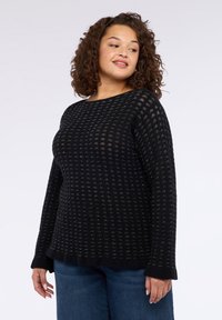 Černý pletený svetr s texturovaným vzorem, kulatým výstřihem a dlouhými rukávy. Kombinováno s modrými džíny s volným střihem.
