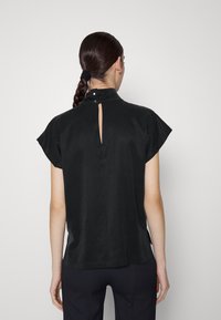 Haut noir à manches courtes avec un col haut, fermeture arrière à boutons et une petite fente. Tissu doux et coupe décontractée, avec des fentes sur les côtés à l'ourlet.