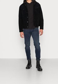 Chaqueta de pana negra con sudadera negra con capucha, jeans azul ajustados y botas negras con cordones. Textura suave y diseño sencillo.