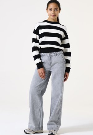 Pull rayé noir et blanc avec texture côtelée ; jean en denim large gris clair ; le mannequin porte des baskets grises. Fond uni.
