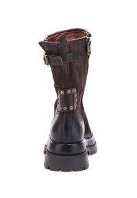 Bota de cuero marrón hasta la rodilla con un diseño arrugado, suela gruesa negra, acentos de hardware dorado y remaches decorativos metálicos en el costado.