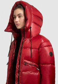 Rode pufferjack met hoge kraag en oversized capuchon, voorzien van een ritszak en zwarte accenten. Glad, glanzend materiaal.