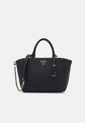 Černá tkaná kabelka s dvojitými uchy, zlatým řetízkovým popruhem přes rameno, štítkem s logem Guess a odpovídající visačkou na jednobarevném bílém pozadí.
