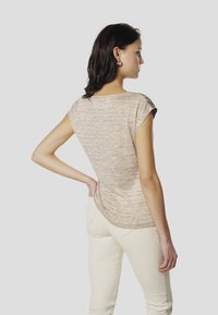 Bēša īsām piedurknēm blūze ar teksturētu apdari, apaļu kakla izgriezumu un nedaudz vaļīgu piegriezumu, kopā ar gaišu, piegulošu biksēm.