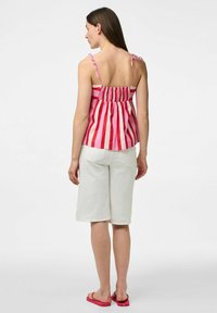 Top senza maniche a righe rosse e bianche con spalline regolabili e schiena arricciata, abbinato a pantaloni corti bianchi fino al ginocchio e infradito rosa.