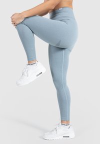 Jasnoniebieskie legginsy prążkowane z wysokim stanem, zestawione z białymi sneakersami z widoczną wkładką powietrzną.