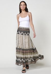 Maxi rok met gestreepte lagen in zwart, wit en aardetinten; lichtgewicht stof; gedragen met een witte tanktop en zwarte sandalen.
