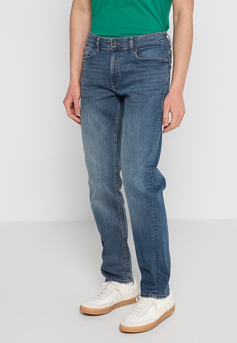 Jeans de denim azul con corte recto, diseño de cinco bolsillos y un desvanecimiento sutil. Costuras semitransparentes y detalles de herrajes metálicos.
