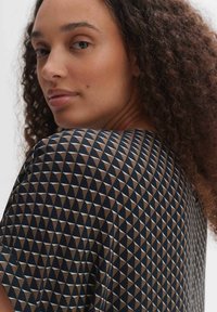Top a maniche corte con un motivo geometrico a triangoli nei colori blu navy, beige e bianco. Tessuto morbido e vestibilità rilassata.