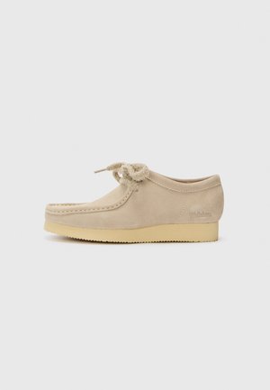 Scarpa in suede beige con punta tondeggiante, lacci decorativi annodati e suola in crepe di gomma beige. Dettaglio del logo discreto sul lato.