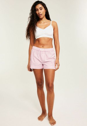 Kvinde stående barfodet iført hvid bralette og lyserøde og hvide stribede shorts med hjerte-detalje på taljebåndet.