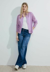 Light purple striped button-up shirt over a white tank top, paired with blue wide-leg jeans and white sneakers. Simple design, casual fit.