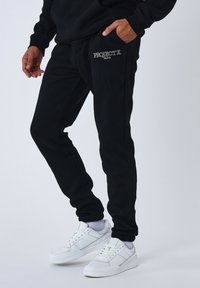 Pantalones jogger negros hechos de material suave, con una cinturilla elástica, bolsillos laterales y un logotipo plateado en el bolsillo izquierdo.